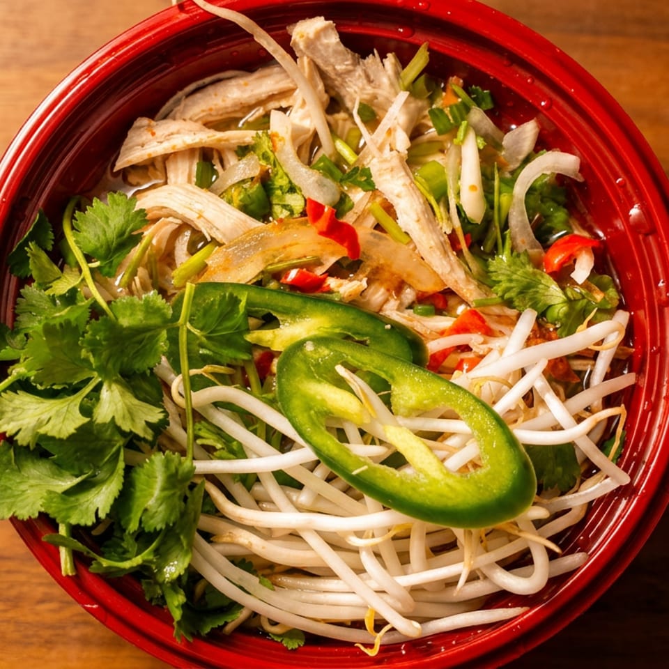Top-down view of a red bowl filled with pho, garnished with cilantro, bean sprouts, and jalapeños.