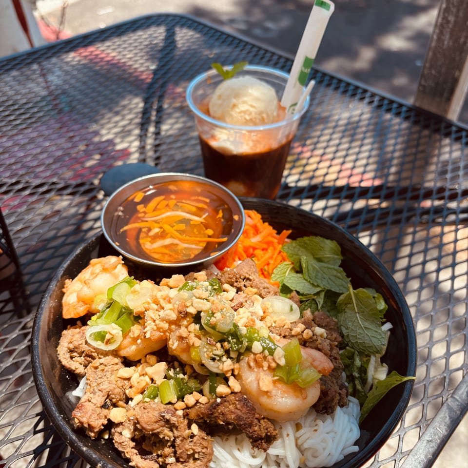 Vietnamese vermicelli bowl with beef, shrimp, peanuts, and herbs, plus an iced coffee float on an outdoor table.