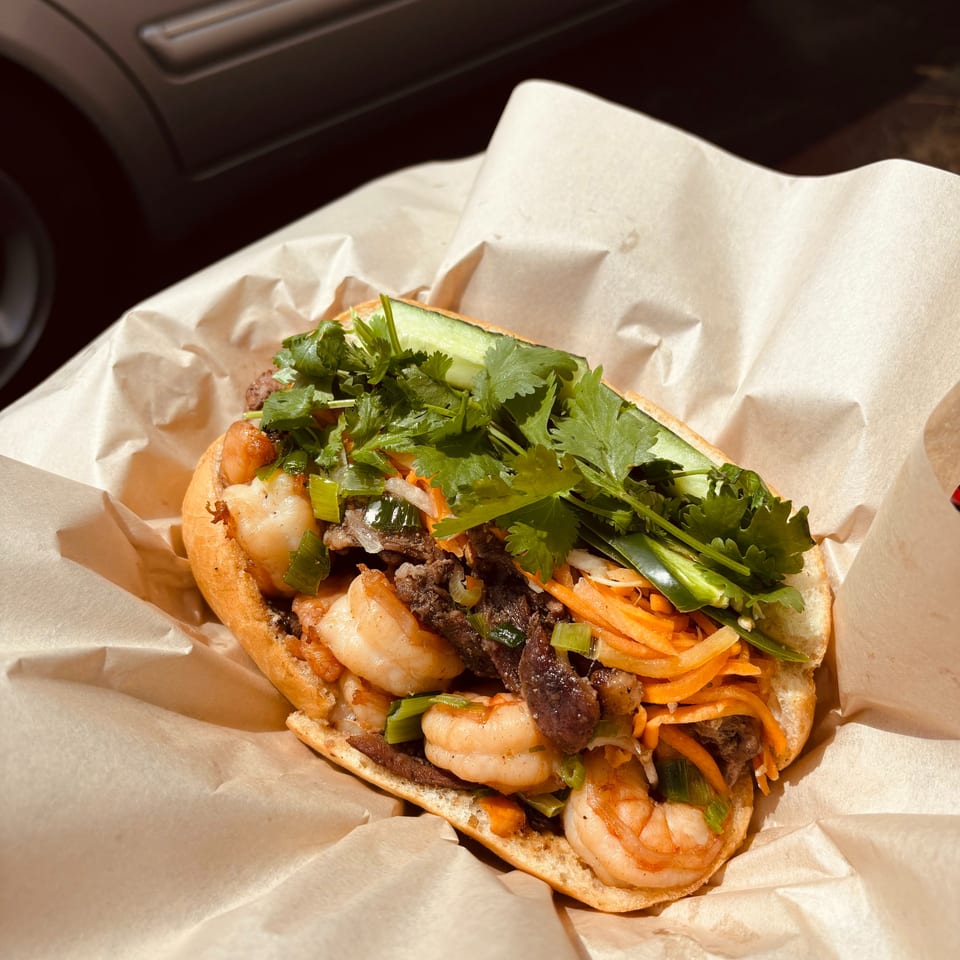 Shrimp and beef banh mi with cilantro, carrots, and cucumber, wrapped in paper.