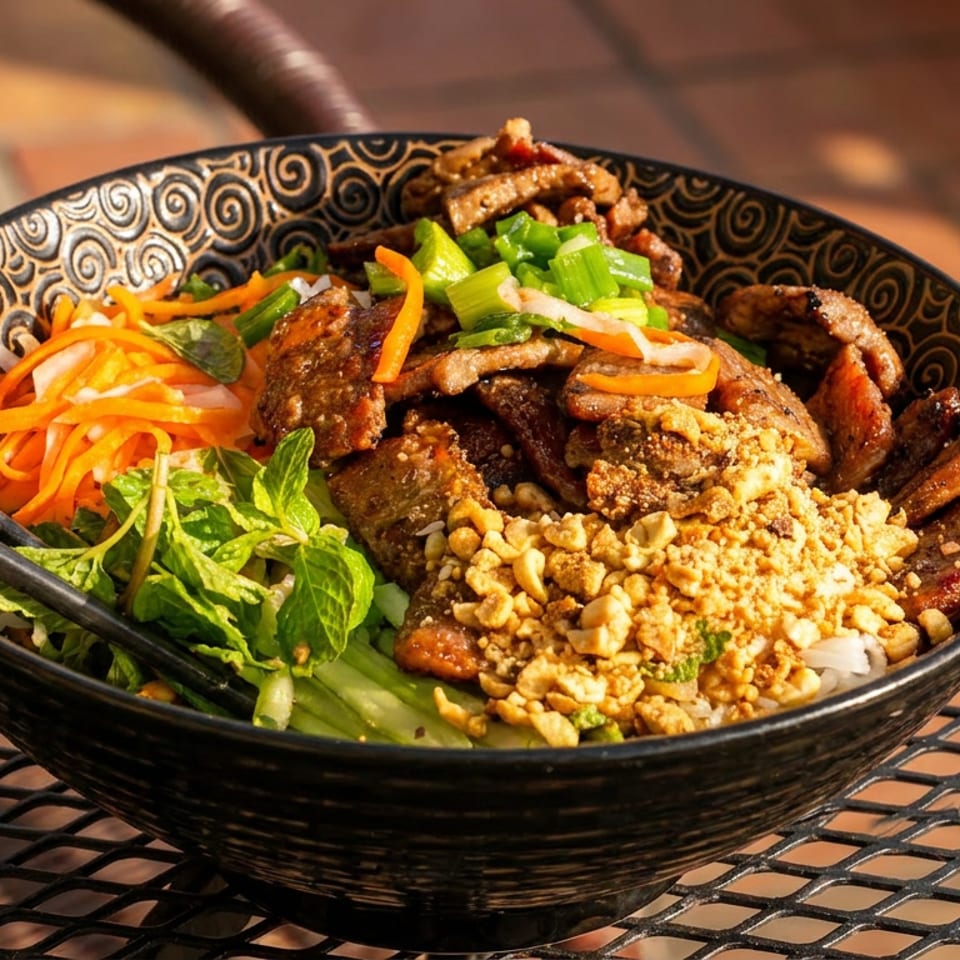 A colorful bowl of Vietnamese vermicelli with grilled pork, peanuts, carrots, and mint, with chopsticks.