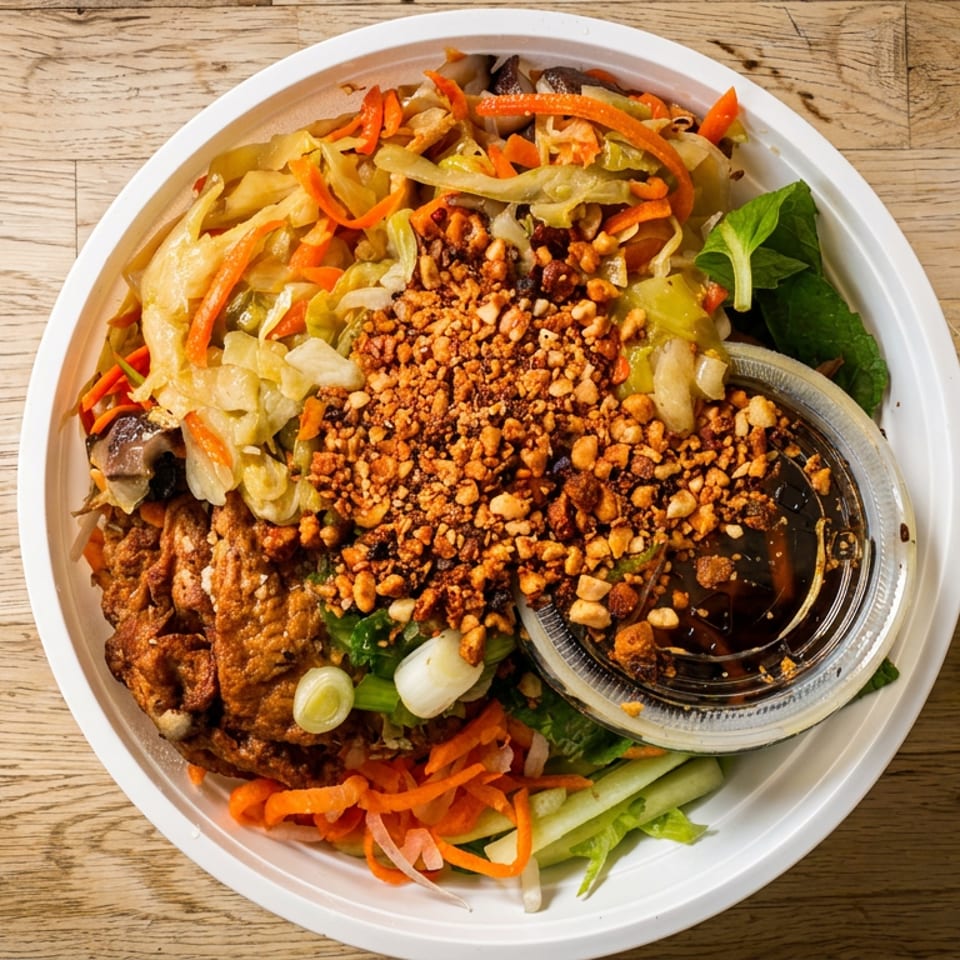 Overhead view of a colorful Asian noodle bowl with vegetables, tofu, peanuts, and sauce.