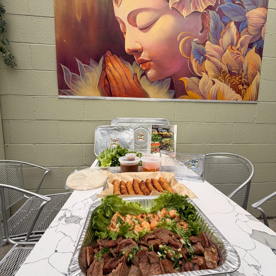 Catering spread with beef, shrimp, lettuce, egg rolls, sauces, and wraps on a marble table.